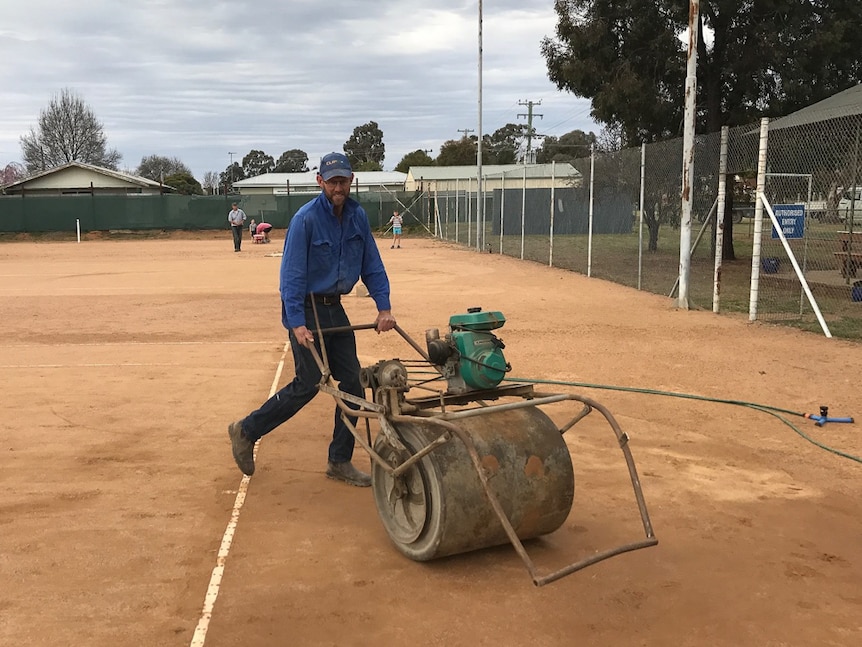 A man using a rolling machine on a clay tennis court.