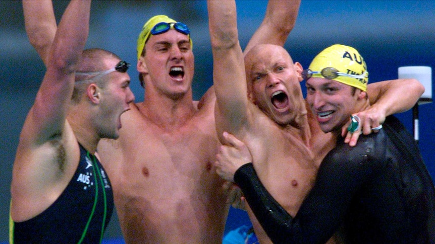 Swimming relay team punches the air and roars in triumph on the blocks after winning Olympic gold.