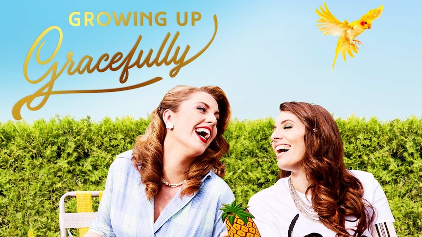 Hannah and Eliza from Growing Up Gracefully sitting in garden laughing, with yellow bird flying in sky