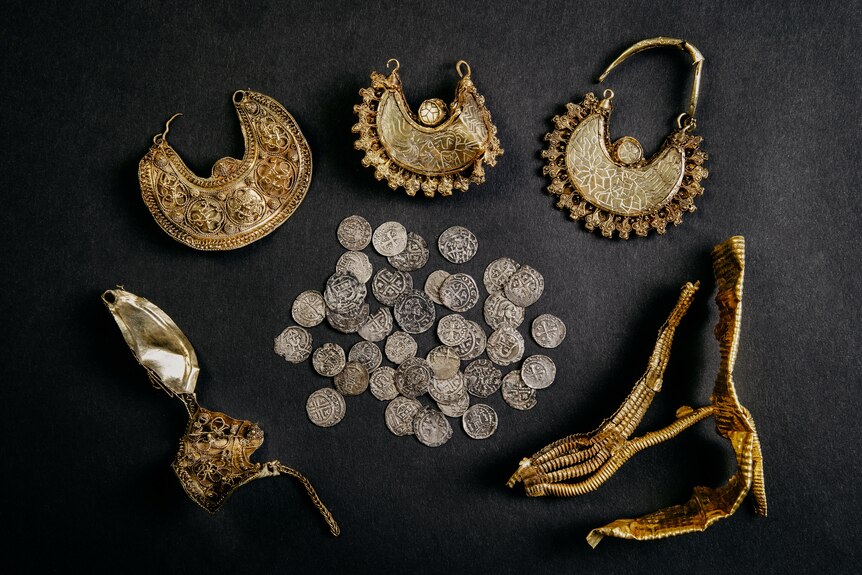 An image of silver coins and golden jewelry with a black background. 