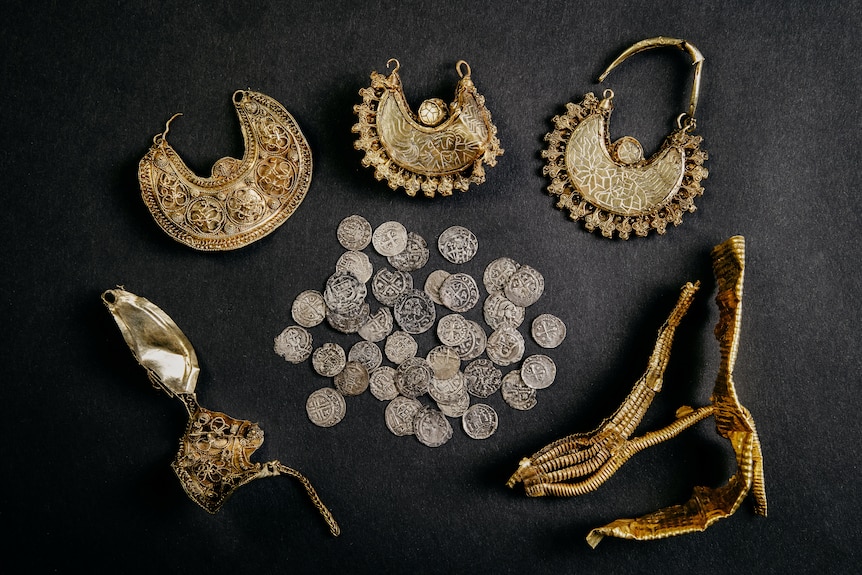 An image of silver coins and golden jewelry with a black background. 