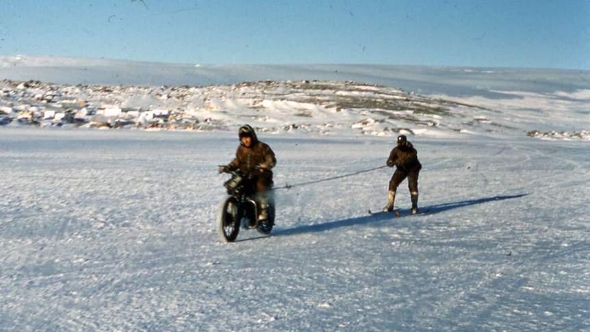 George Cresswell riding his velocette motorbike in Antarctica, towing a skier behind him