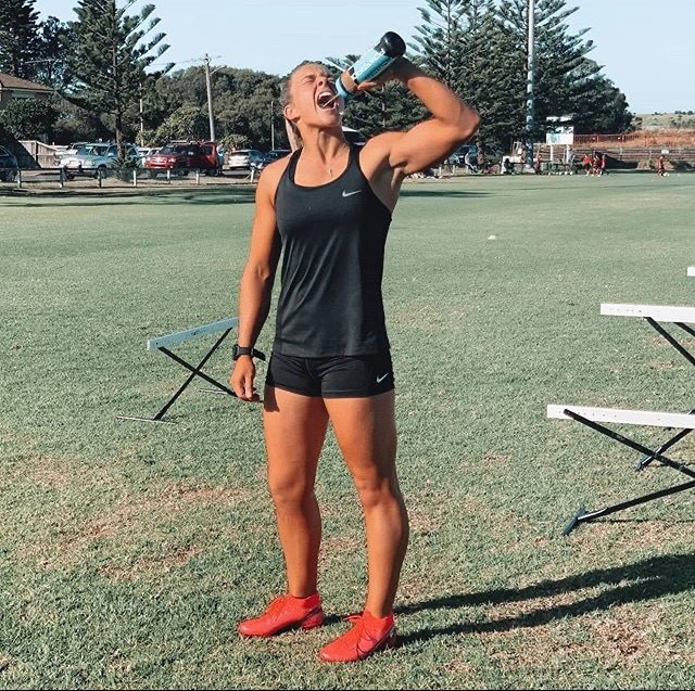 Karra-Lee Nolan stands on a field and drinks from a water bottle.