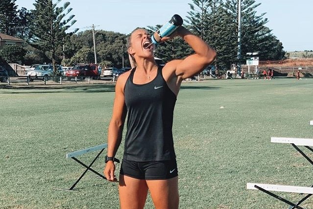 Karra-Lee Nolan stands on a field and drinks from a water bottle.