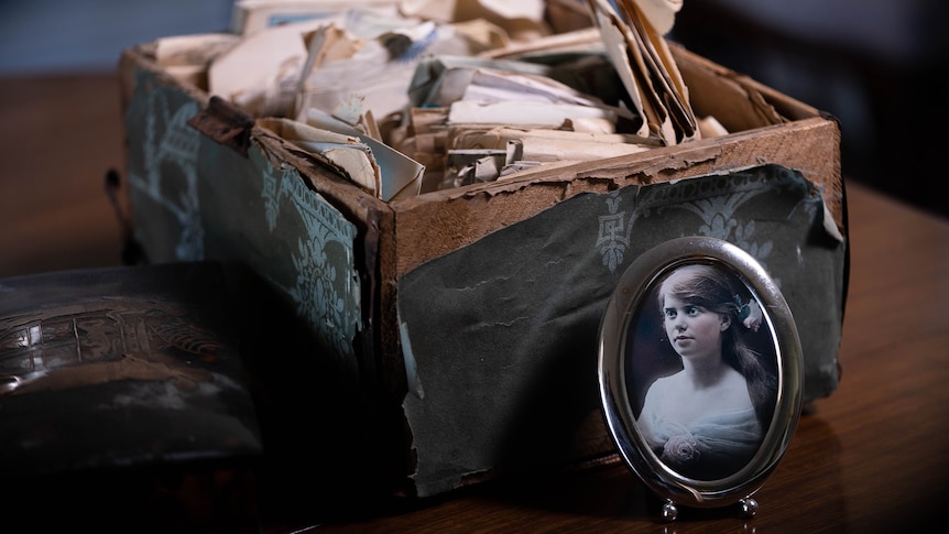 A small oval frame of a woman leaning on a box of old letters