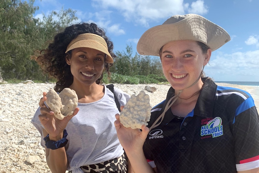 Two women stand on a coral beach.