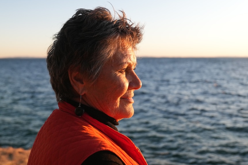 A 71-year-old woman looks out at the blue sea. The setting sun is drenching her face.   