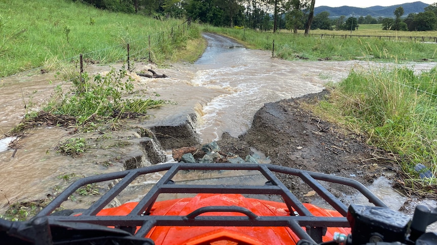 A photo over the front of a quad bike looking at a farm road cut by floodwater.