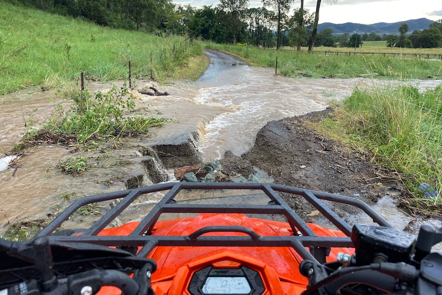 A photo over the front of a quad bike looking at a farm road cut by floodwater.