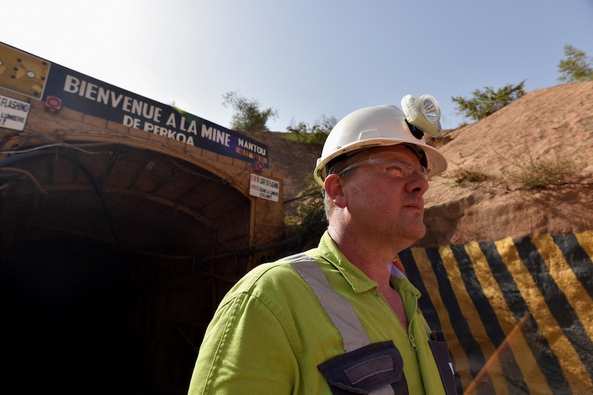 a man in a mining helmet and high vis vest outside a mine entrance