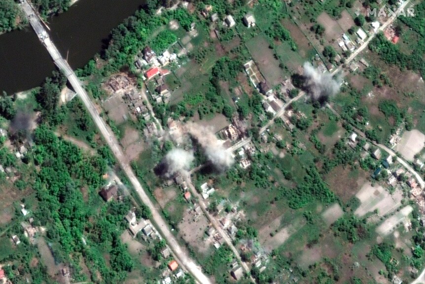 A satellite image showing plumes of dark smoke rising from multiple points across a town. 