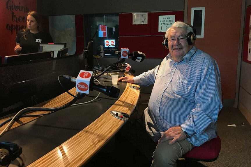 Photograph of a man in a stripy short in a radio studio. He is smiling at the camera