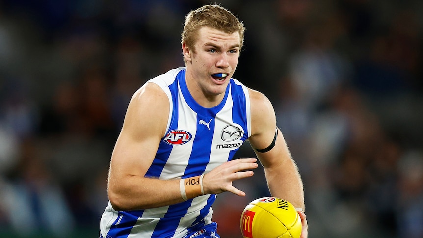 A North Melbourne AFL player runs with the ball during a 2022 match.
