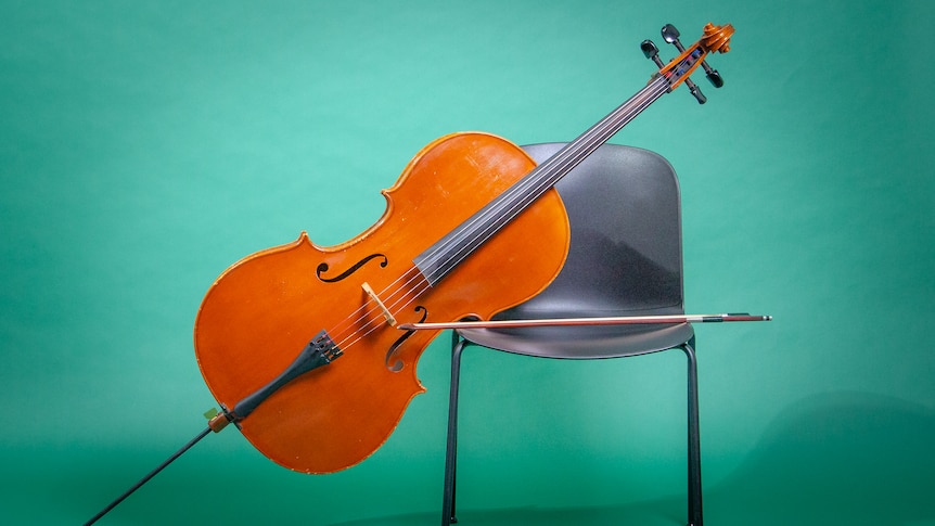 A cello leans against a black chair on an angle with the bow lying across the chair. The is a blue background.
