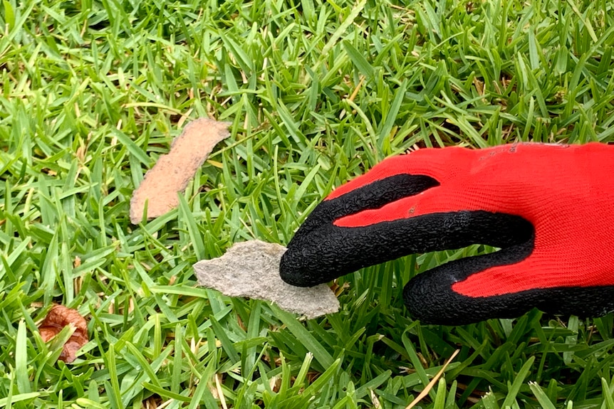 a golved hand hold a large piece of asbestos material.