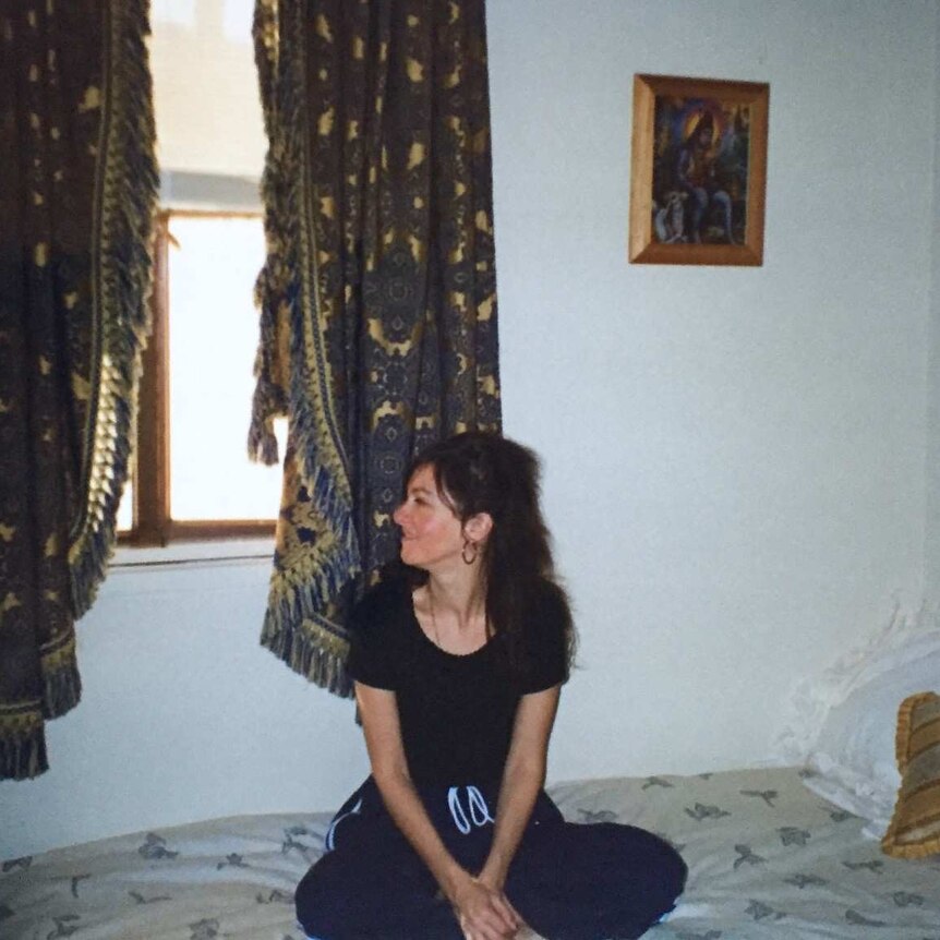 Tanya-Lee Davies sits on her bed in her room at the ashram. A spiritual painting hangs on the wall.