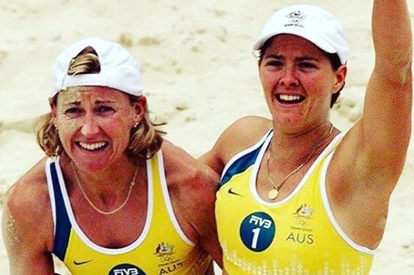 Two women wearing yellow and green bikinis embrace on the sand.