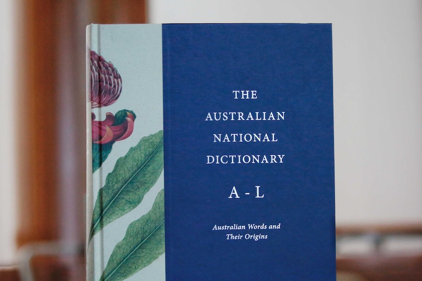 A navy blue book titles the Australian National Dictionary stands on a table