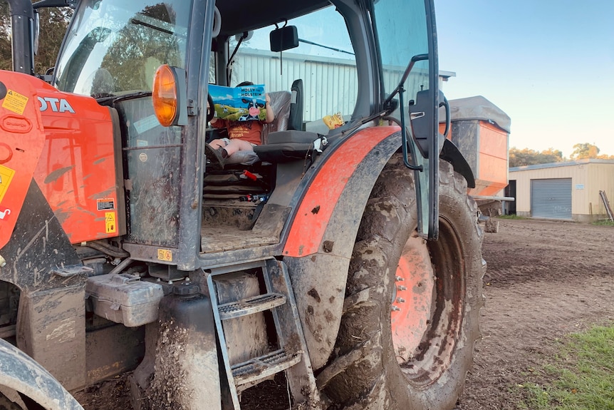 Young boy sits in big, orange tractor reading holly the holstein book