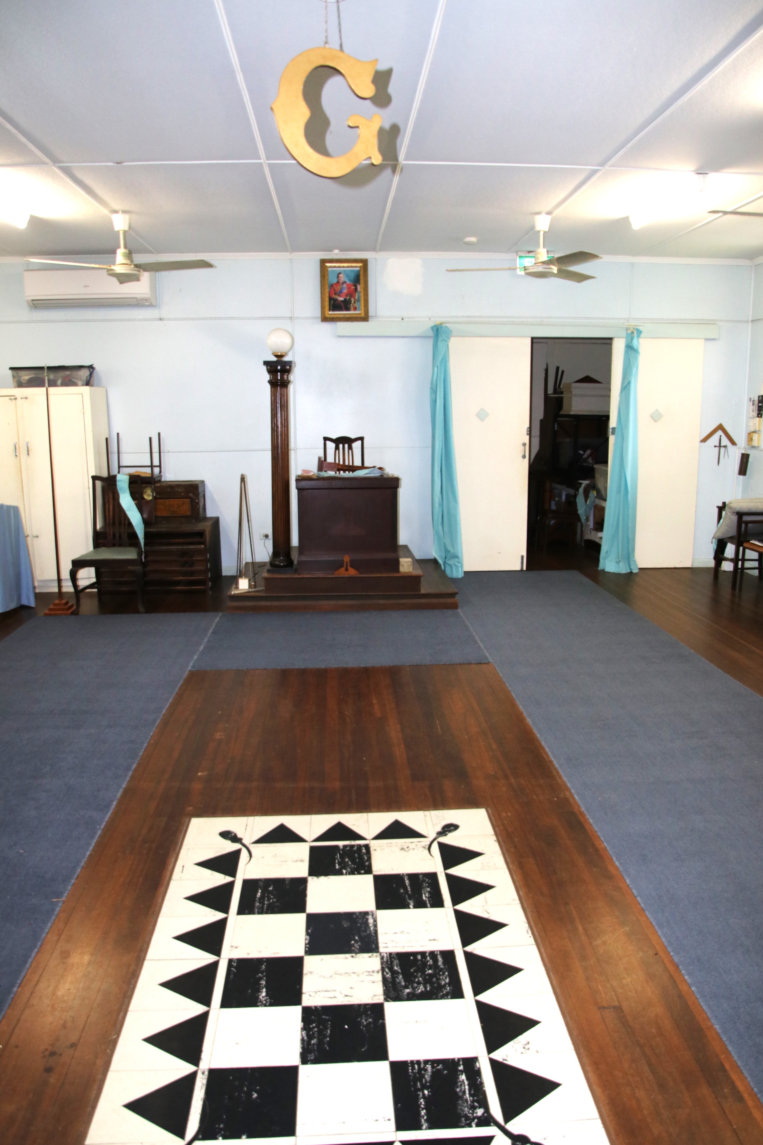 A room with a checkerboard floor and a giant G hanging from the ceiling 