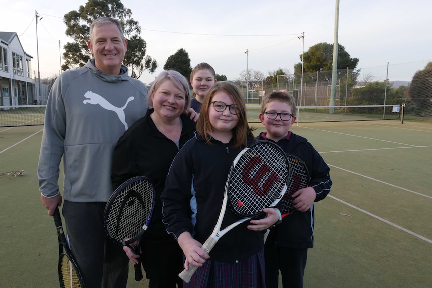 A family of five holding tennis rackets and smiling at the camera