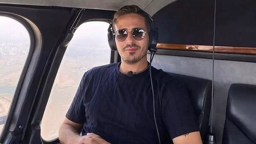 Man sits in helicoper looking directly at camera with glasses and slight smile. 
