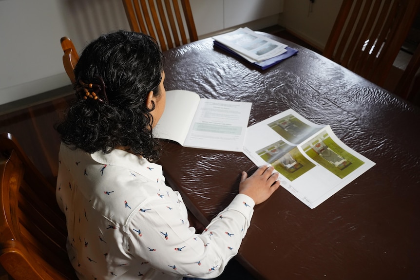 Looking down from behind Rebecca looking at building plans on her dining table. 