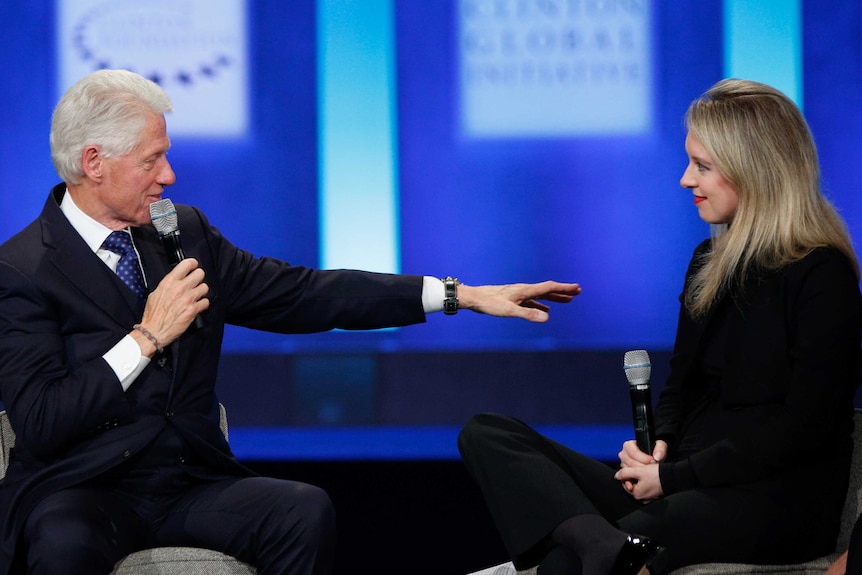A man gestures to a woman on a conference stage.