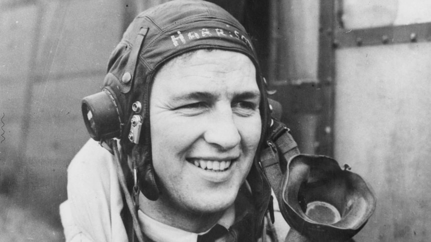 Portrait of a smiling man in a leather flying helmet with 'Harrison' painted on it and and unclipped oxygen mask.