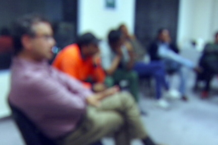 A group of men sitting around a circle on chairs, their images are blurred.
