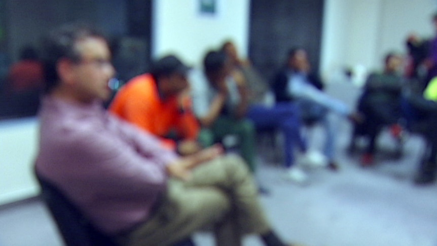 A group of men sitting around a circle on chairs, their images are blurred.