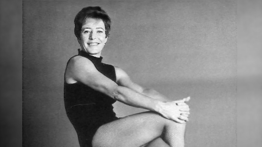 A woman in a black leotard sits smiling.