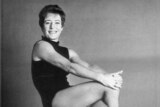 A woman in a black leotard sits smiling.