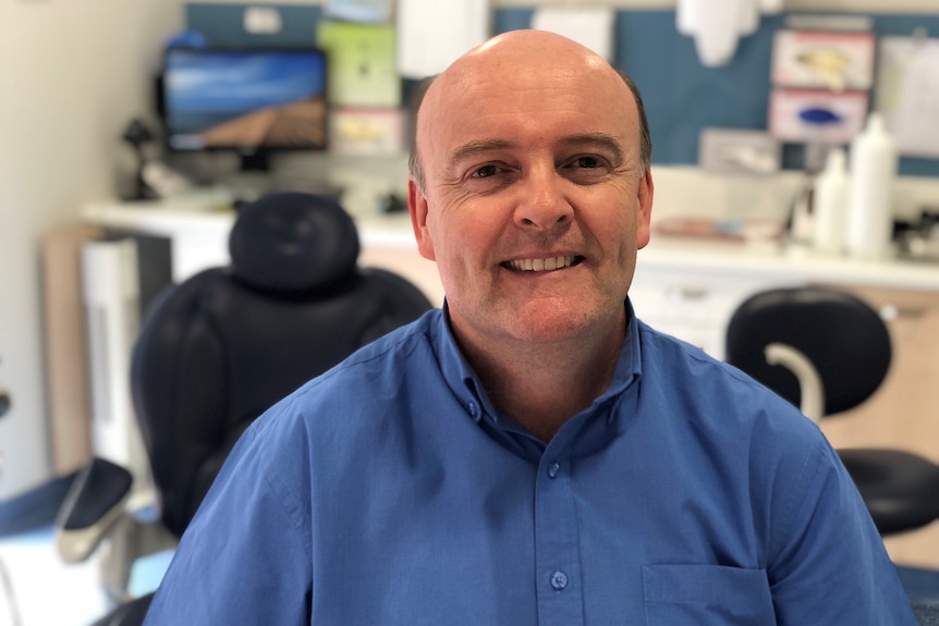 Man smiling seated in front of dentist's chair. 