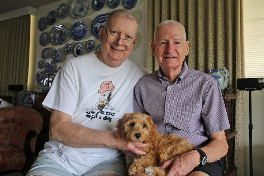 Mr Ebert with husband John sit together in their East Brisbane apartment with their new puppy on their lap.