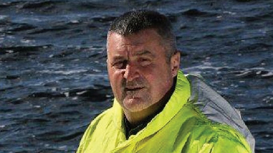 Man in yellow raincoat holds large fish by the gills on a boat at sea, Tasmania