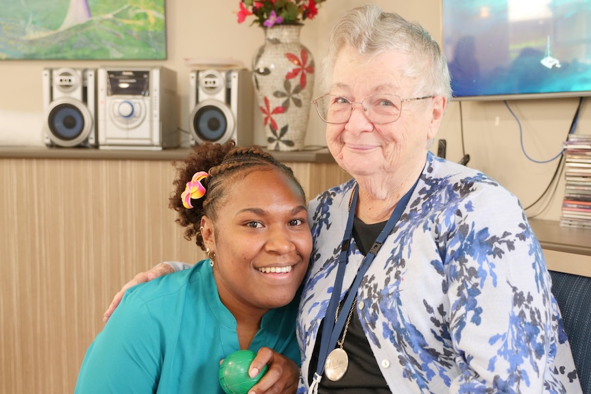 A woman from Vanuatu hugs an older woman at an aged care home, both smiling.