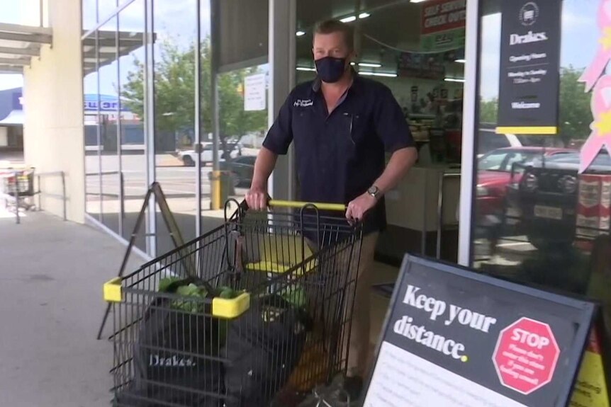 A man wearing a black face mask pushes a trolley out of a supermarket