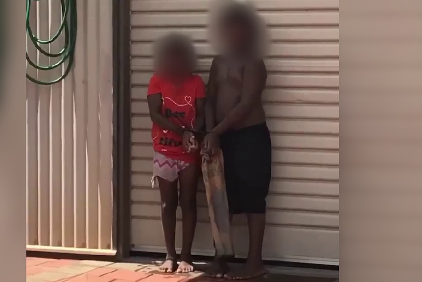 Two children bound at the hands with zip ties, standing against a garage door. 