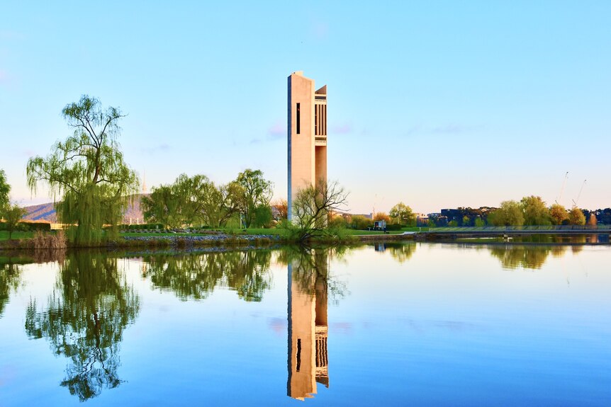 A large pillar stands on the shore of a gleaming lake with the structure reflected in the water