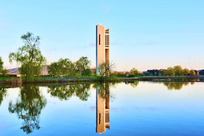 A large pillar stands on the shore of a gleaming lake with the structure reflected in the water