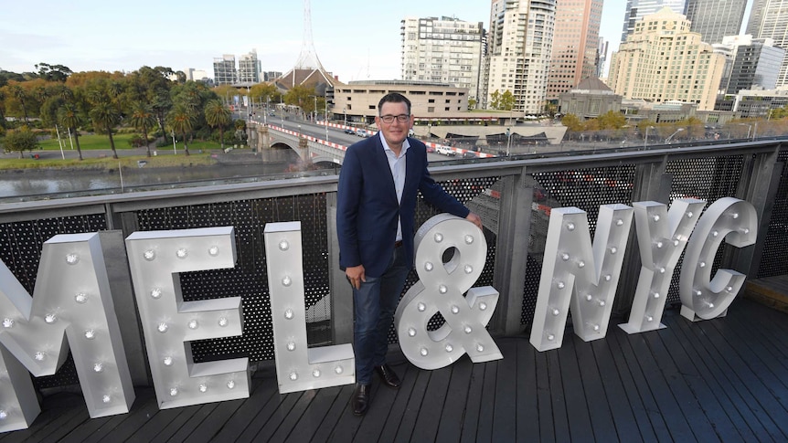 Daniel Andrews stands with large letters spelling out M E L & N Y C.