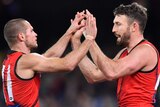 Two male AFL players congratulate each other on a goal by giving a high five.