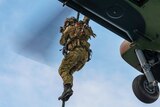 A soldier in camouflage uniform rappels from a helicopter.