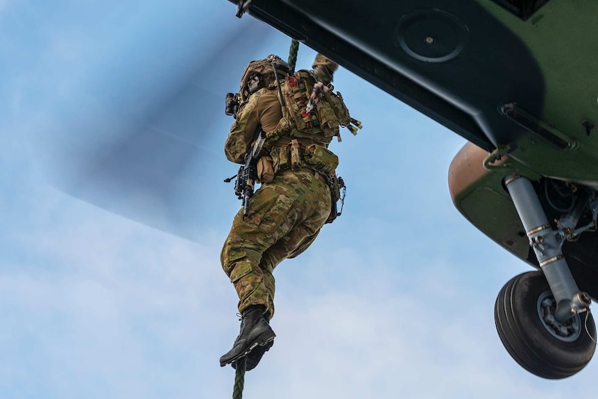 A soldier in camouflage uniform rappels from a helicopter.