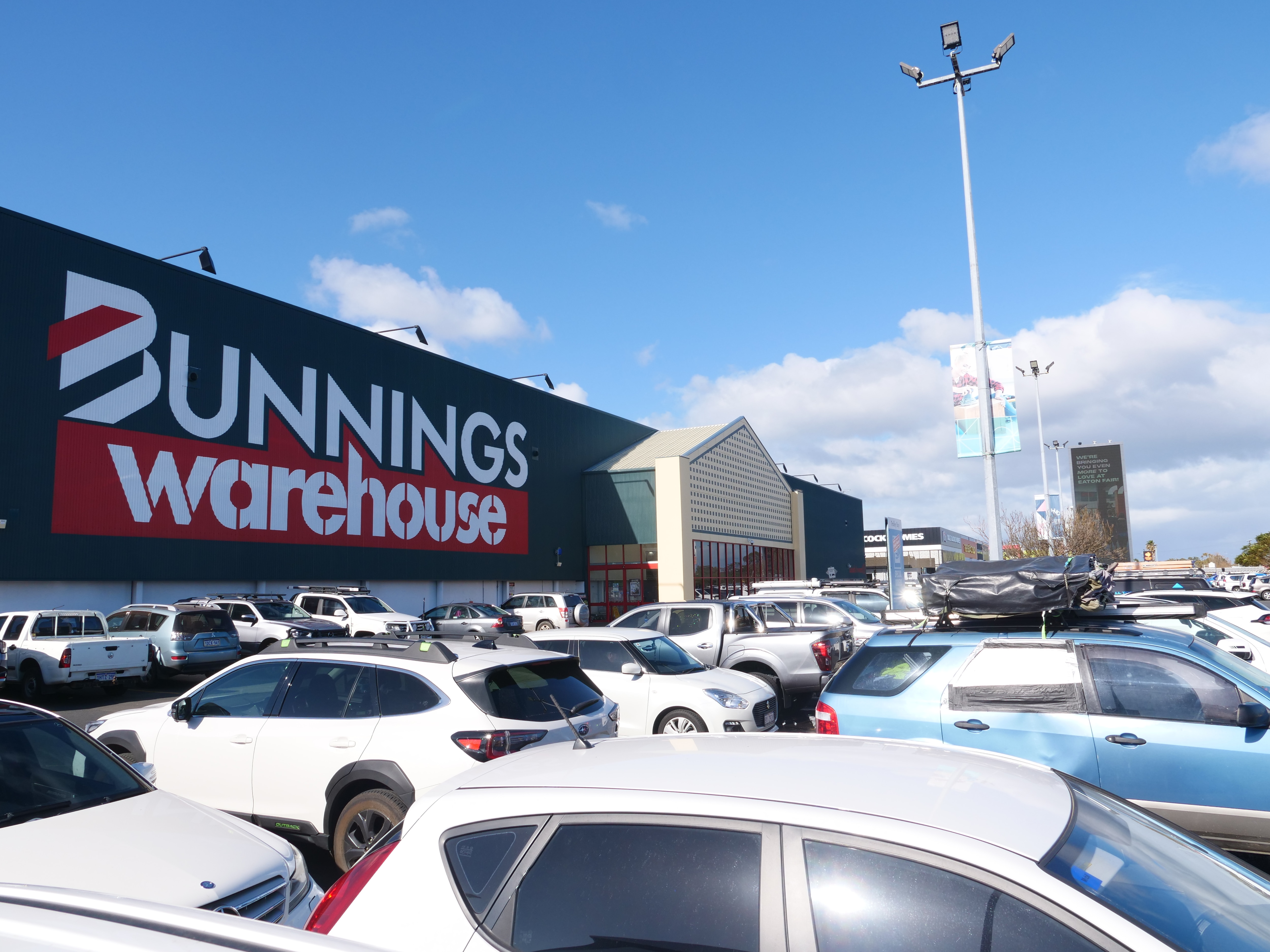 The outside of a Bunnings store, large warehouse building with lots of cars in the carpark.