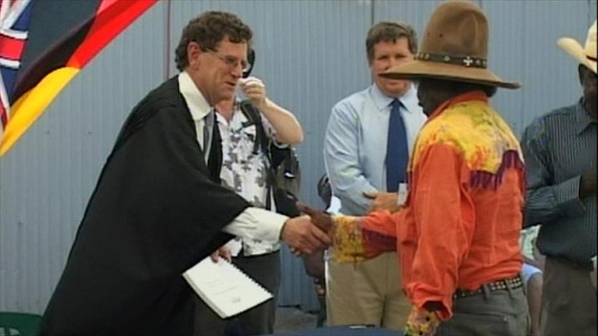 Indigenous man shakes hands with a judge (?) at a ceremony