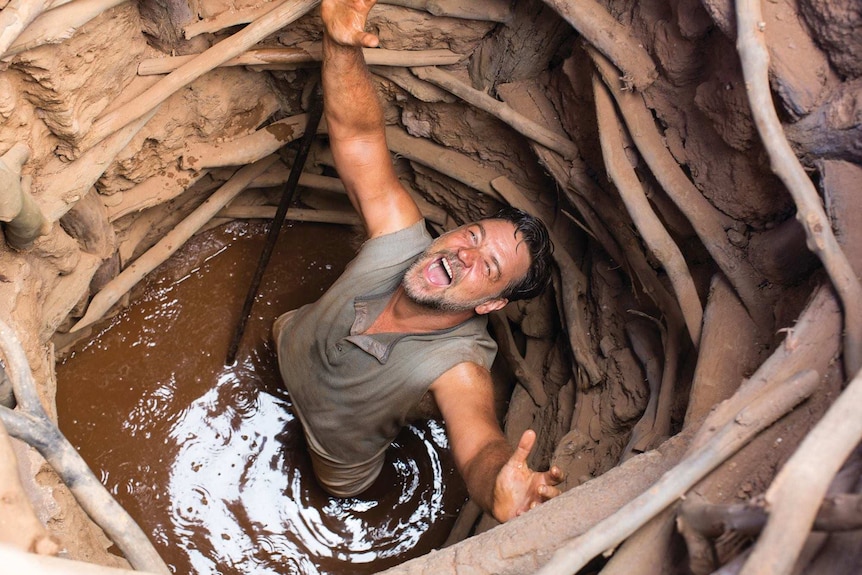 A man celebrates finding water at the bottom of a well in outback Australia.