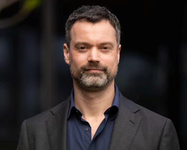 Dr James Martin in a black shirt looks at the camera