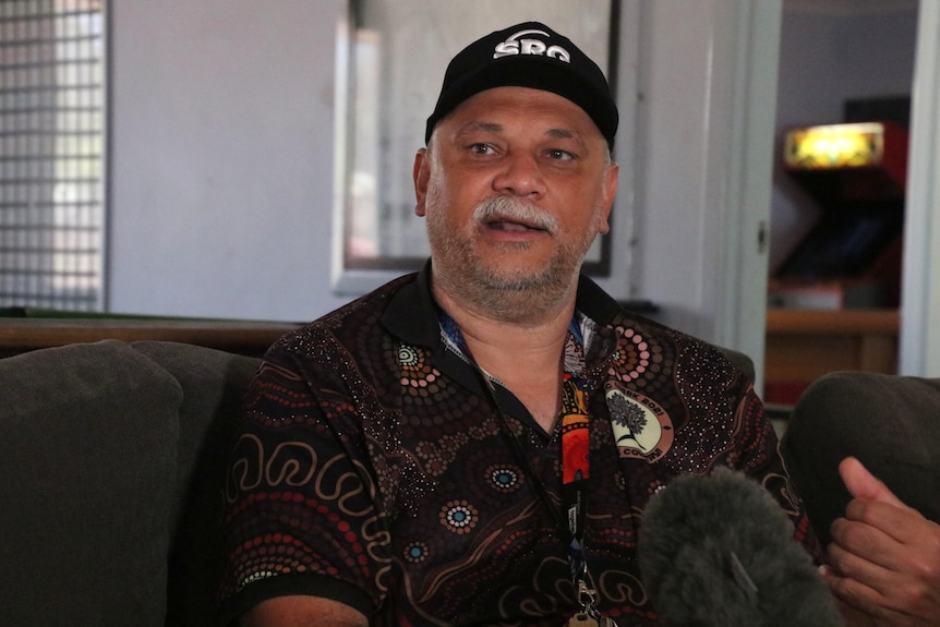 An Indigenous man sits on a couch as he is interviewed